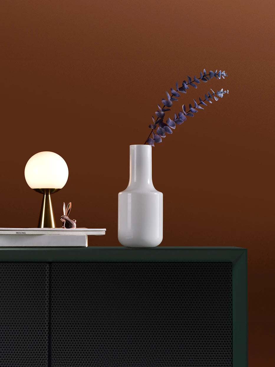 Vintage wabi furnishing shot of white minimalist vase A with dried purple eucalyptus on dark green perforated sideboard against warm brown wall