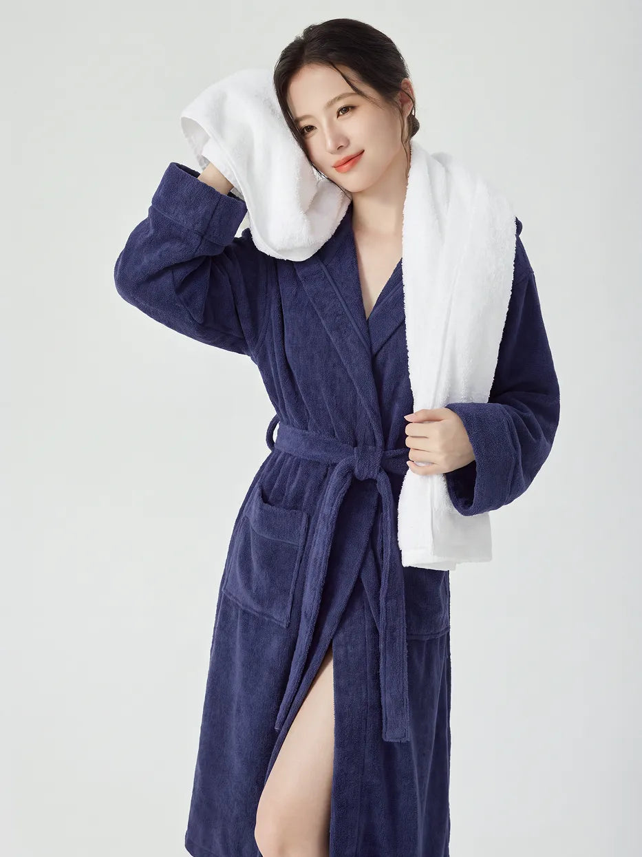 Woman wearing RESONG navy blue hooded terry cloth bathrobe, draping a white cotton bath towel over shoulder and gently pressing towel corner against cheek, luxury bath towel and bathrobe gift set, white studio background
