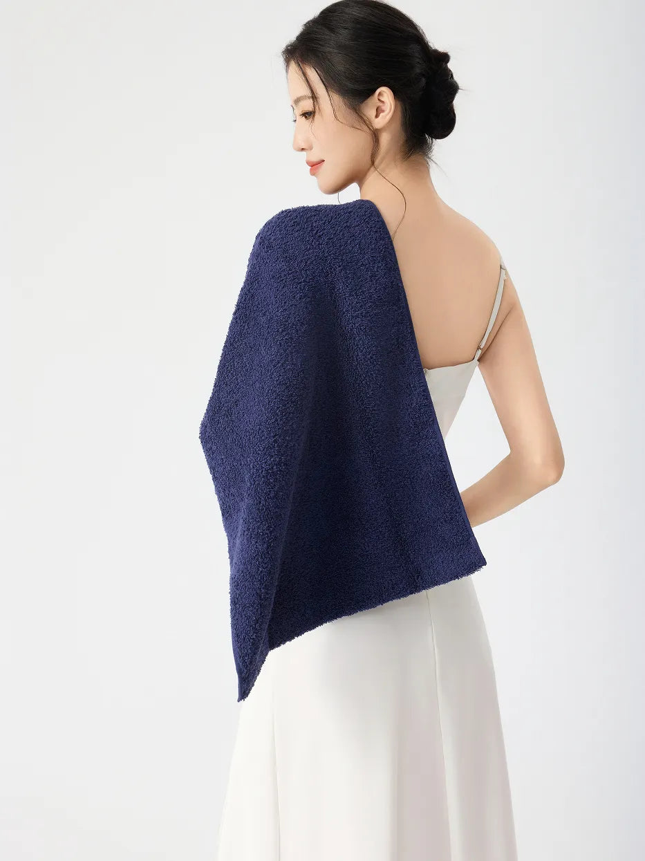 Woman in side back view draping RESONG navy blue cotton terry face towel over bare shoulder, soft fluffy cotton face towel on model, white slip dress, white studio background
