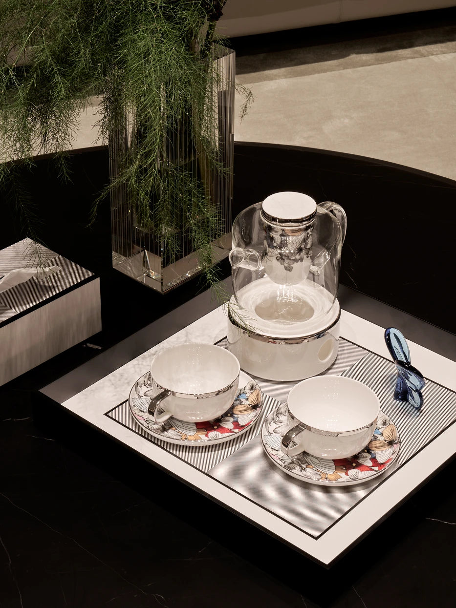 Light luxury living room furnishing shot of large black square tray holding ceramic tea pot & printed mugs on black marble table