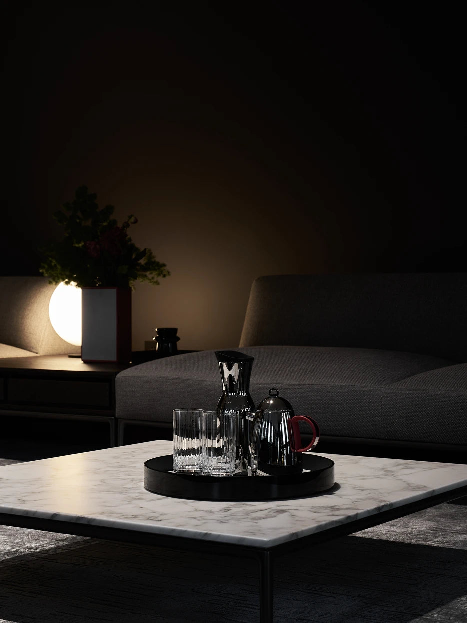 Modern light luxury living room layout shot of large black round tray holding stainless steel moka pot & fluted water glasses on grey-white marble square coffee table