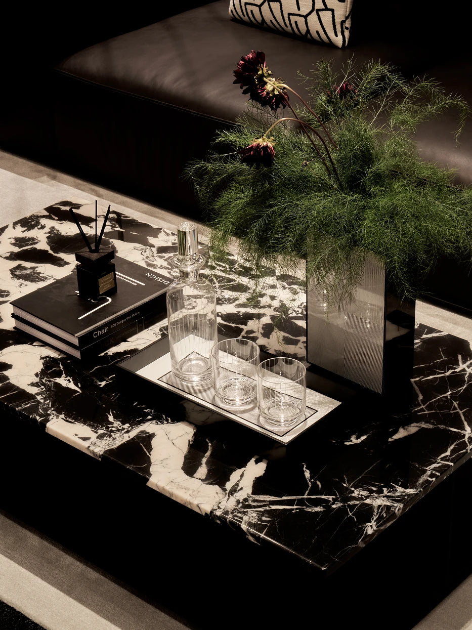 Italian retro reception layout shot of long black tray with glass water bottle & tumblers, matched with perfume and art books on black-white marble table
