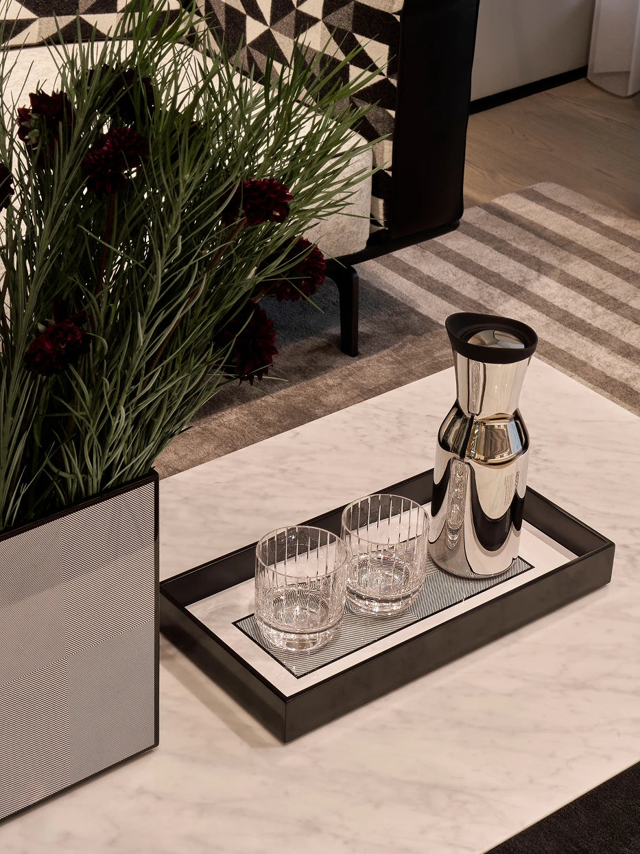 Modern light luxury living room furnishing shot of black long tray with metal water kettle & fluted crystal tumblers on grey-white marble coffee table