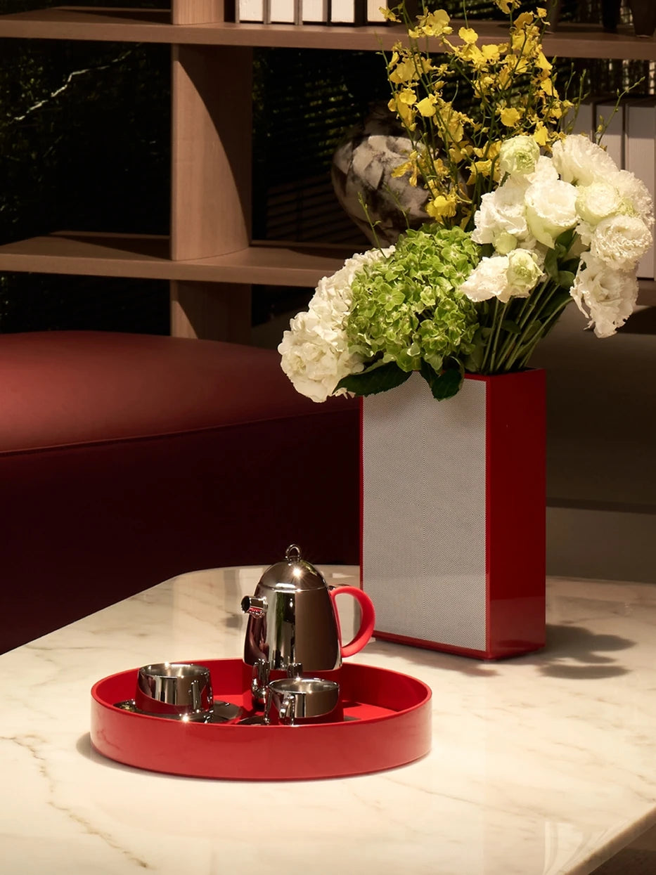 Warm tone furnishing shot of medium red round tray with printed ceramic mug & orange coaster on dark wood table