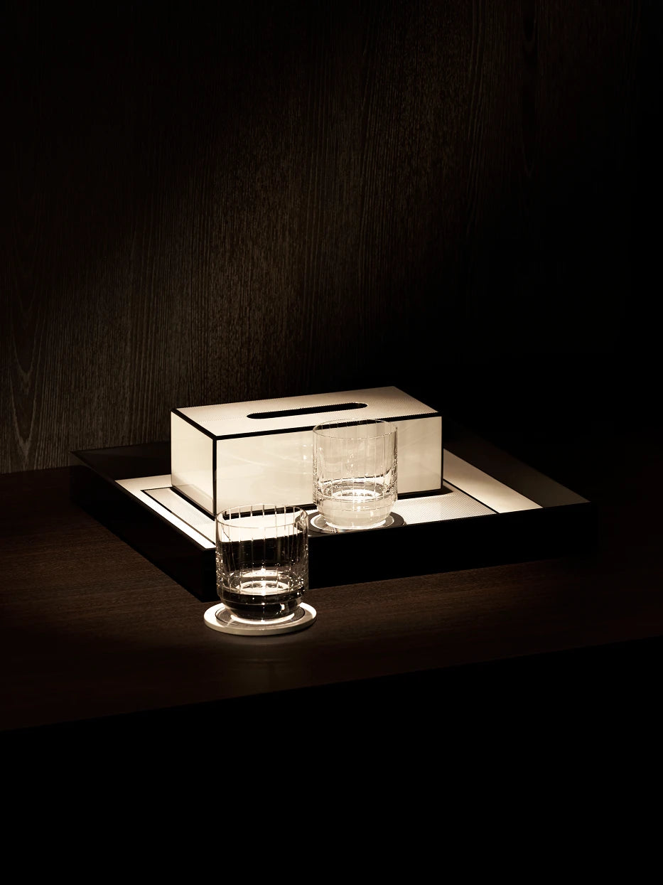 Luxury reception layout shot of tissue box matched with fluted clear glass tumblers and white round coasters on dark solid wood table