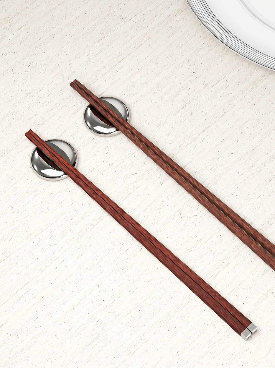 Daily home table layout shot of PAVILION rosewood chopsticks matched with LINGLONG stainless steel chopstick rests on light speckled stone tabletop