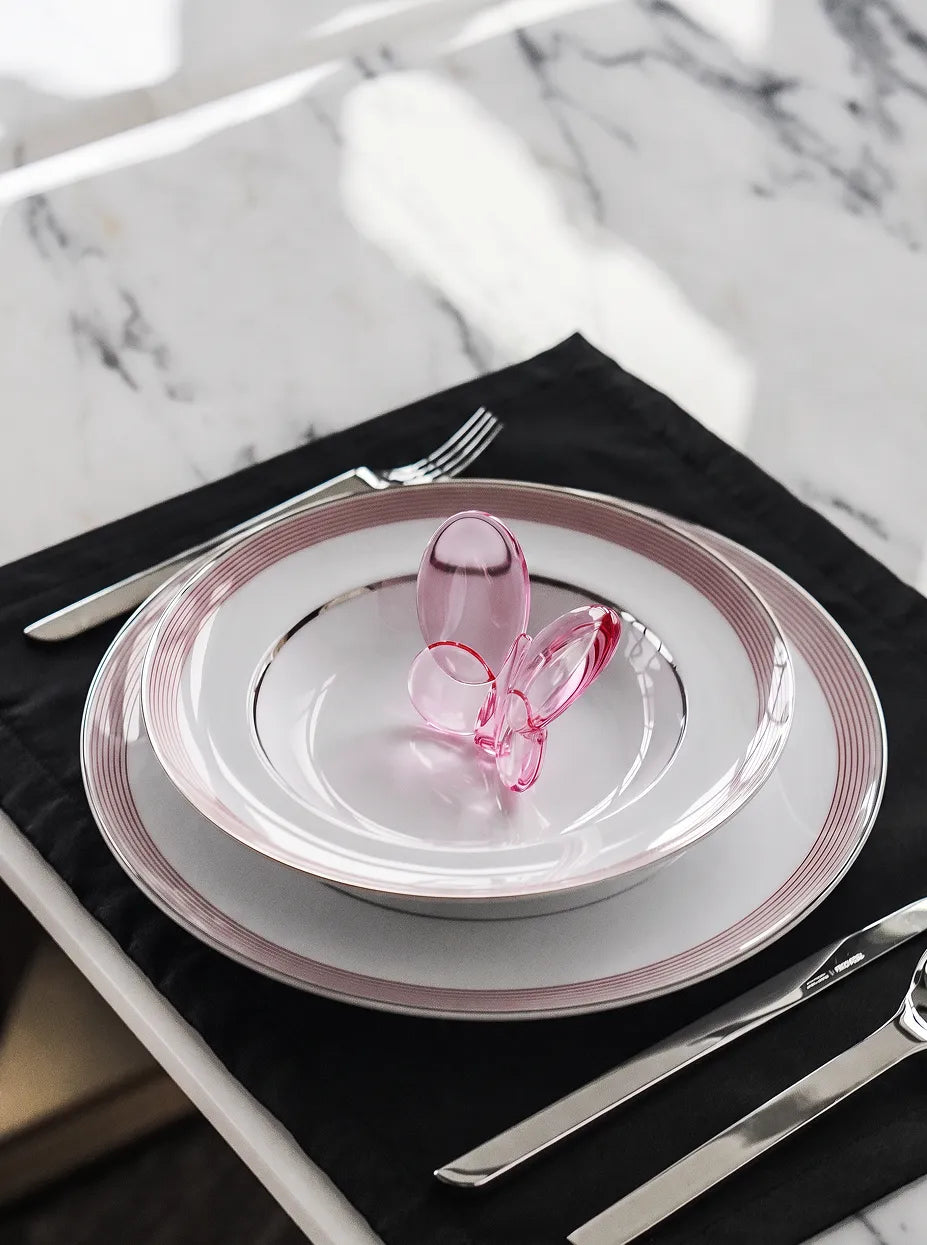 Soft minimalist dining furnishing shot of cherry pink crystal butterfly on double pink-lined ceramic plates over black-white marble table