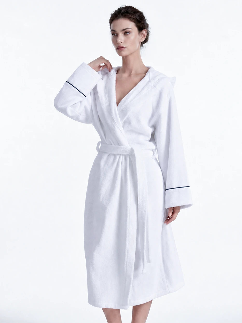 Pure white background full-body side shot of model wearing R Collection white cotton hooded bathrobe, showing loose dropped shoulder long well-fitted silhouette, clear navy contrast piping cuff detail, fluffy soft cotton terry texture, highlighting comfortable water-absorbent wearing experience of 100% cotton