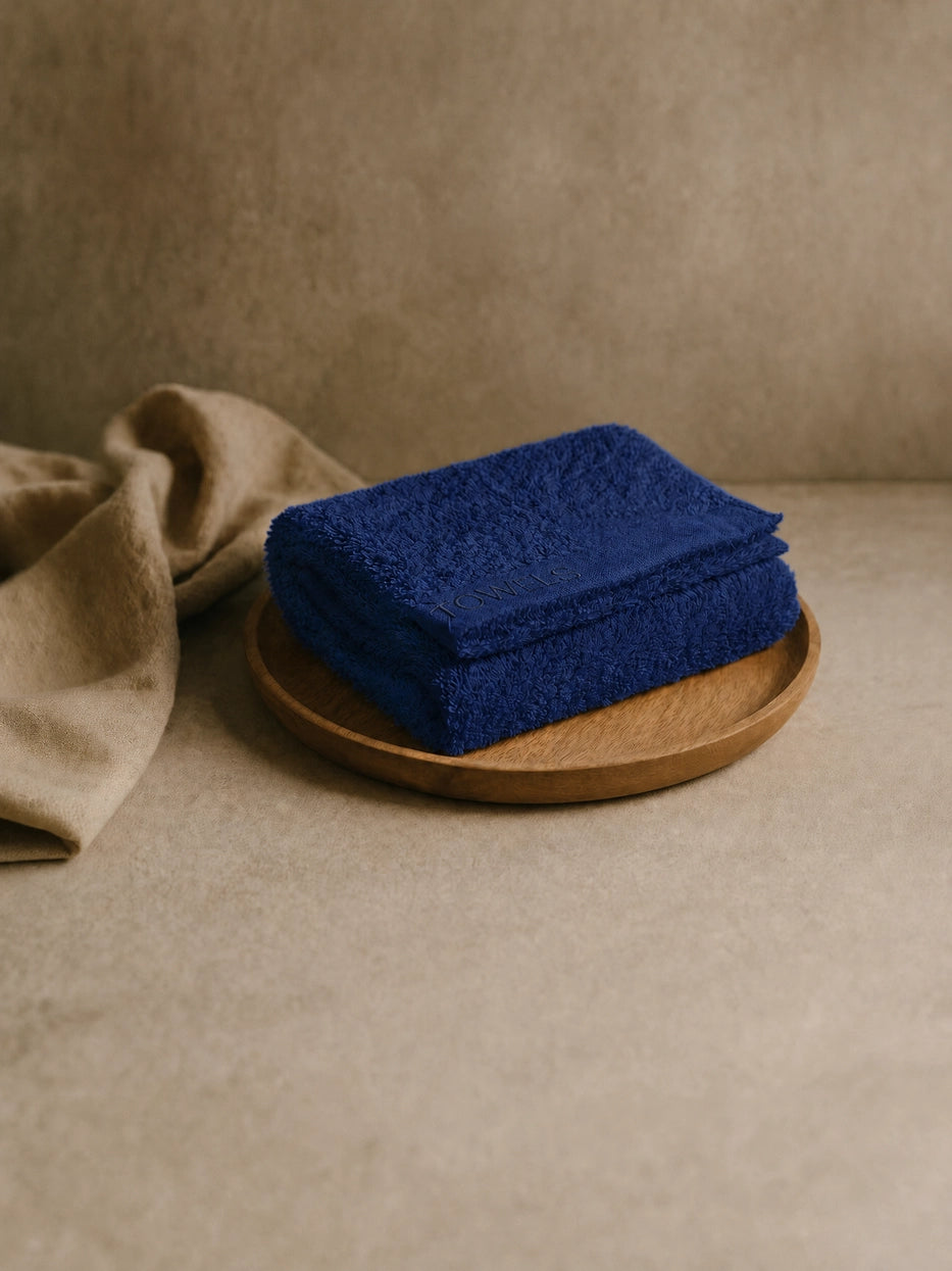 Wabi-sabi still life shot on beige micro-cement countertop with wooden tray, folded navy blue R Collection cotton face towel matched with linen fabric, soft natural light creates calm neutral bathroom atmosphere, shows interior display matching effect