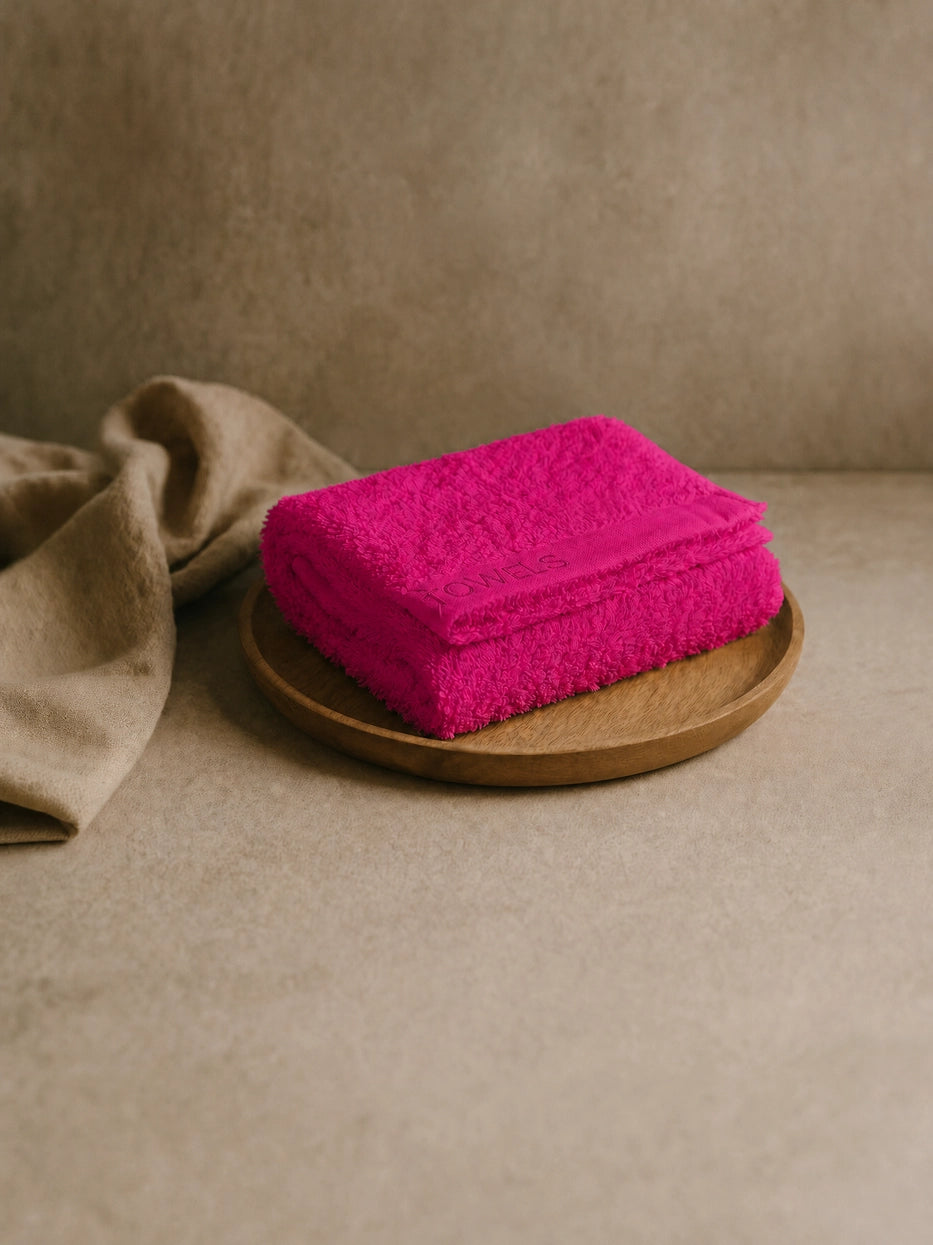 Wabi-sabi still life shot on beige micro-cement countertop with wooden tray, folded rose red R Collection cotton face towel matched with linen fabric, soft natural light creates vibrant bathroom atmosphere, shows interior display matching effect