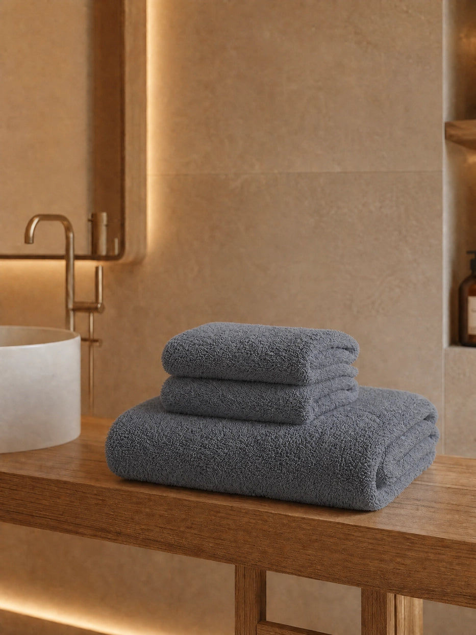 Wabi-sabi warm wood bathroom still life shot of three stacked grey towels on wooden countertop, unified solid grey tone calm and premium, matched with linear ambient light to show minimalist high-end display texture of full gift set