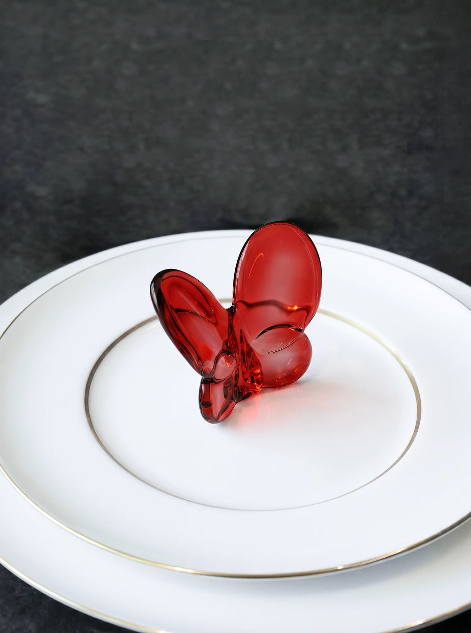 Minimalist dining furnishing shot of red crystal butterfly placed on double-layer gold-rim white ceramic plate on dark matte countertop