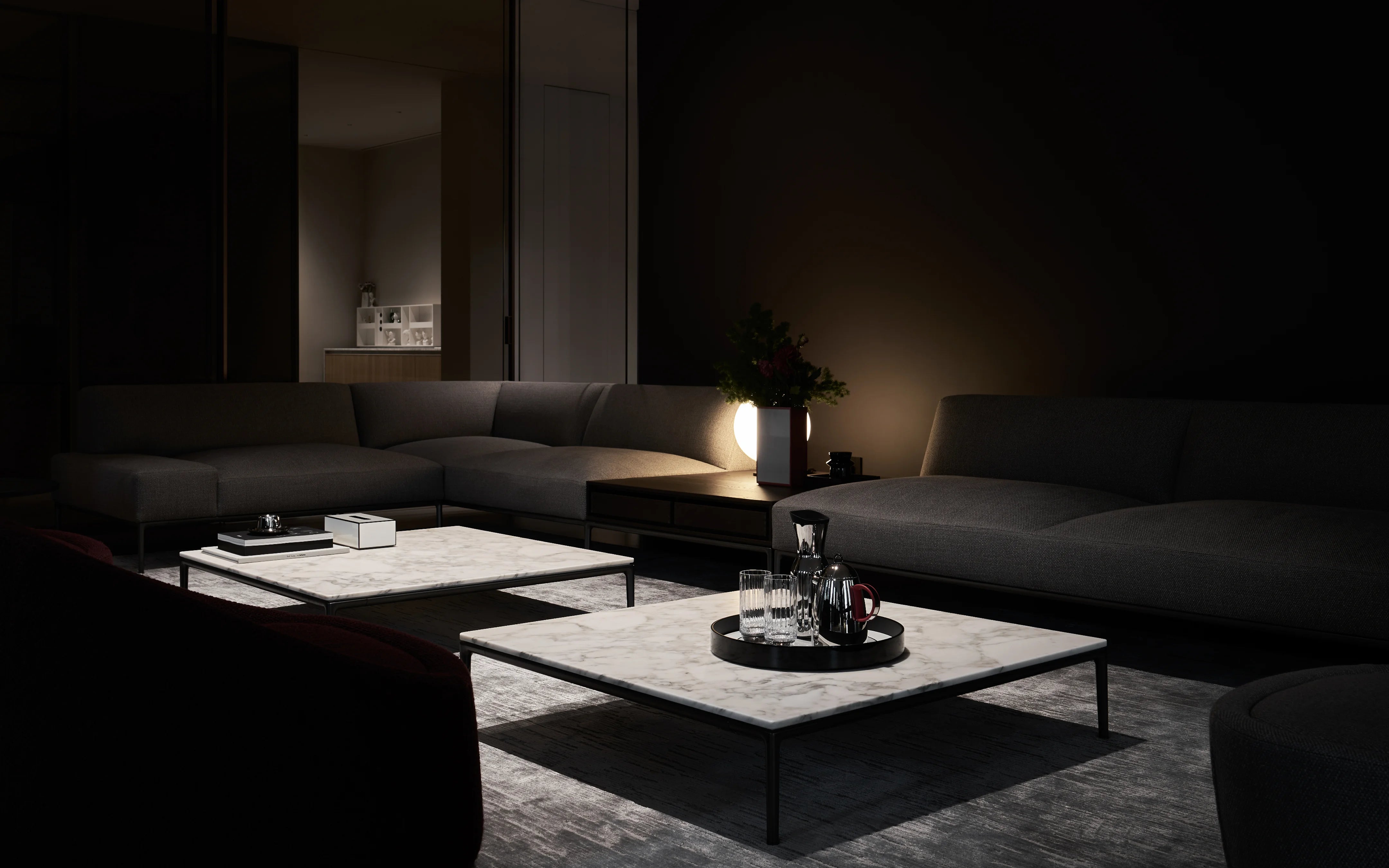 Panoramic lifestyle shot of RESONG HOME full matching set including SHEDI round marble coffee table, GENTLEMAN stainless steel water pitcher & tumblers, OPTICAL ART lacquer vase, dark tone Italian minimalist large flat living room with sectional fabric sofa, dim warm ambient lighting