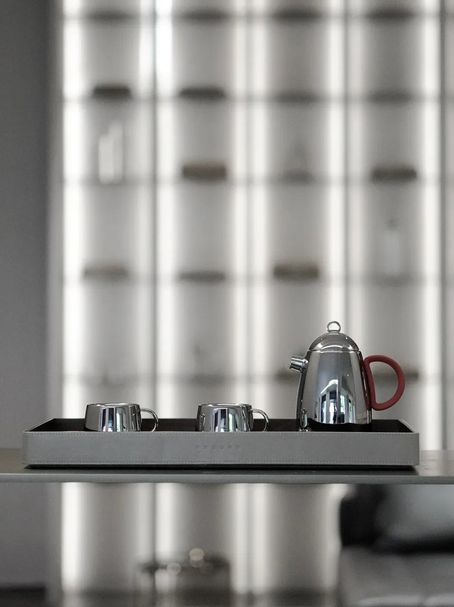 Official lifestyle image of the RESONG SHEDI Red Handle Teapot - S, a mirror-polished stainless steel teapot with matching cups presented on a serving tray for modern tea service.