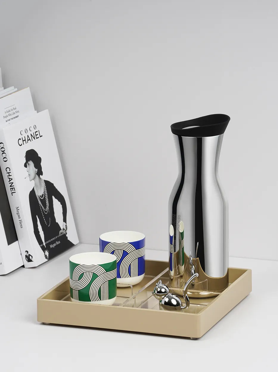 Official lifestyle image of the RESONG SHEDI Water Carafe, a mirror-polished stainless steel water carafe displayed with tea cups on a serving tray for contemporary tea service.