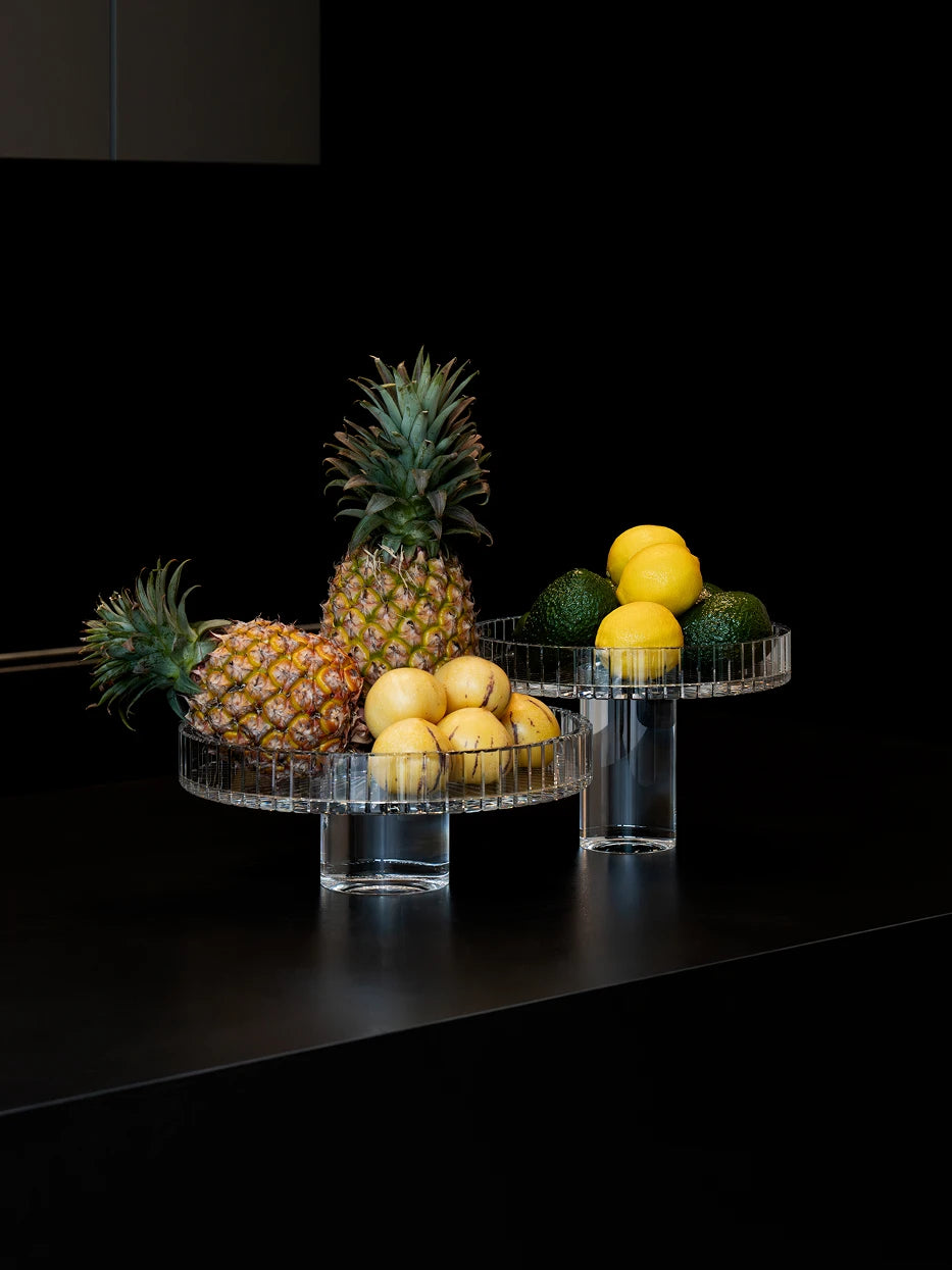 Luxury commercial display shot of large SHIJI L fruit plate full of pineapples & fruits, matched with M plate of avocados and lemons on matte dark stone bar counter