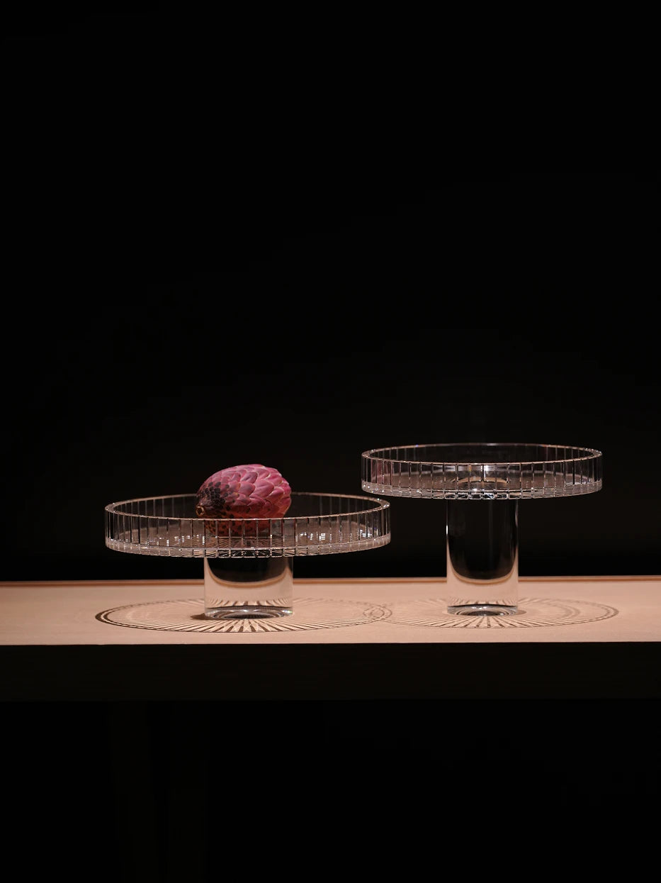 Minimal high-end furnishing shot of staggered SHIJI L & M fruit plates on light wood surface against solid dark backdrop