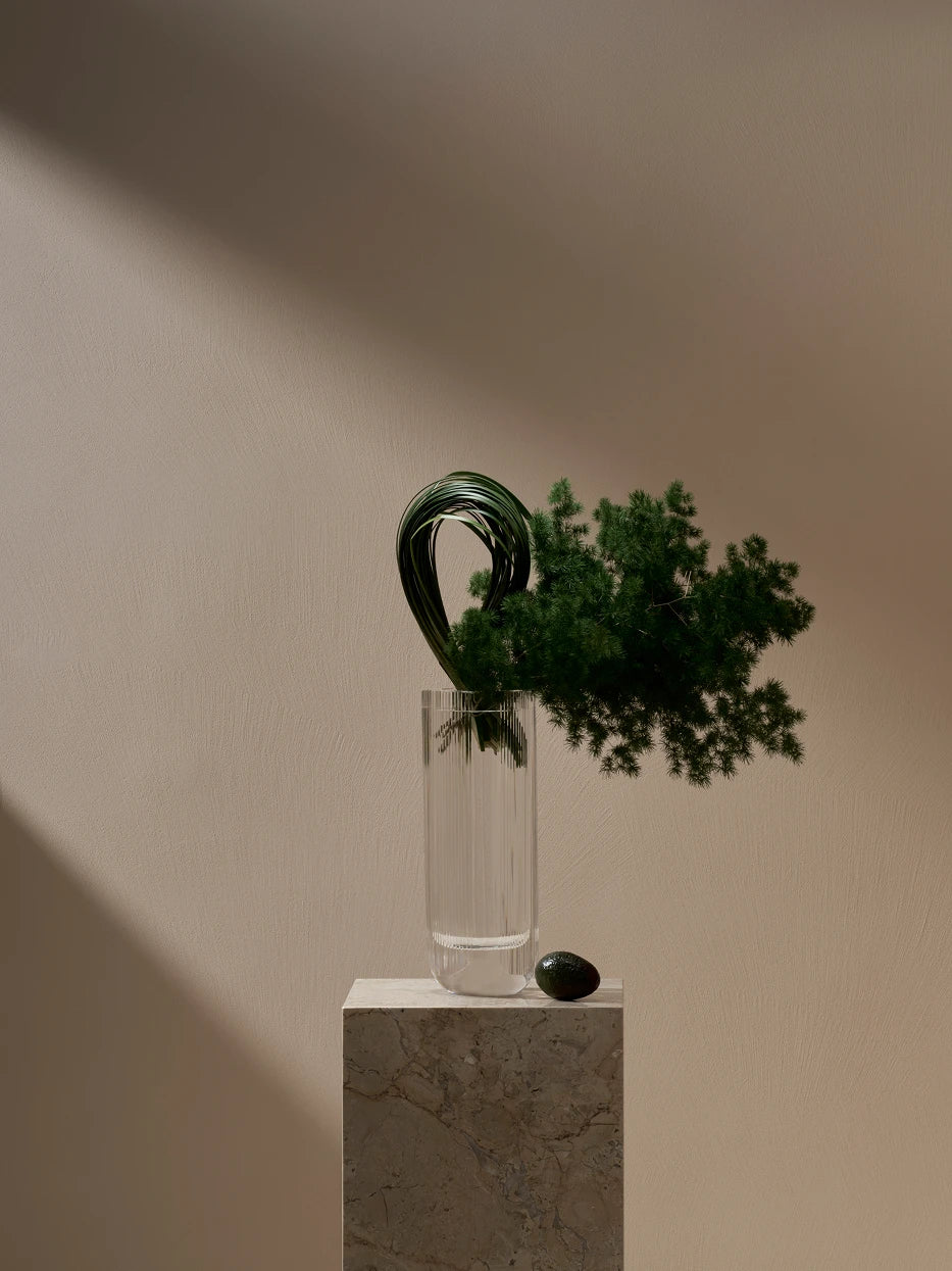 Soft minimalist furnishing shot of SKYSCRAPER slim crystal vase with artistic curved grass & pine foliage on travertine stone display plinth
