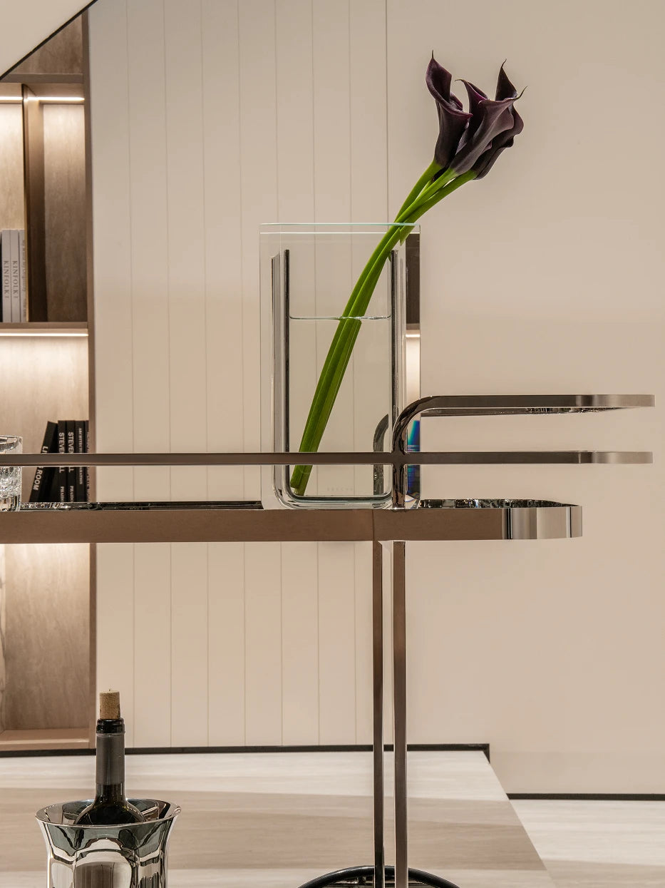 Partial furnishing still life shot of top tray with glass vase, calla lily and wine decanter beside lit built-in bookcase