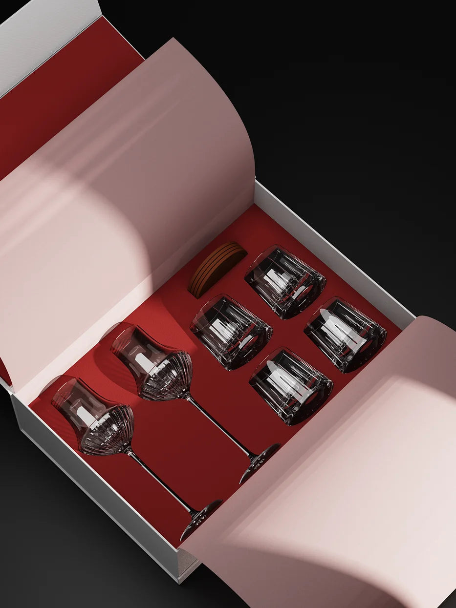 Top-down full interior shot of opened premium gift box for RESONG TRIUMPH Whiskey Collection, includes 2 vertical ribbed crystal wine goblets, 4 geometric cut whiskey tumblers and wooden coasters, neatly placed on red flannel lining against dark background, luxury glass set for home bar, banquet and holiday gifting