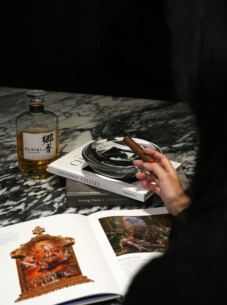 Luxury men's bar layout shot of large WATERDROP L crystal ashtray stacked on art books, matched with whisky bottle and cigar on black-white marble countertop