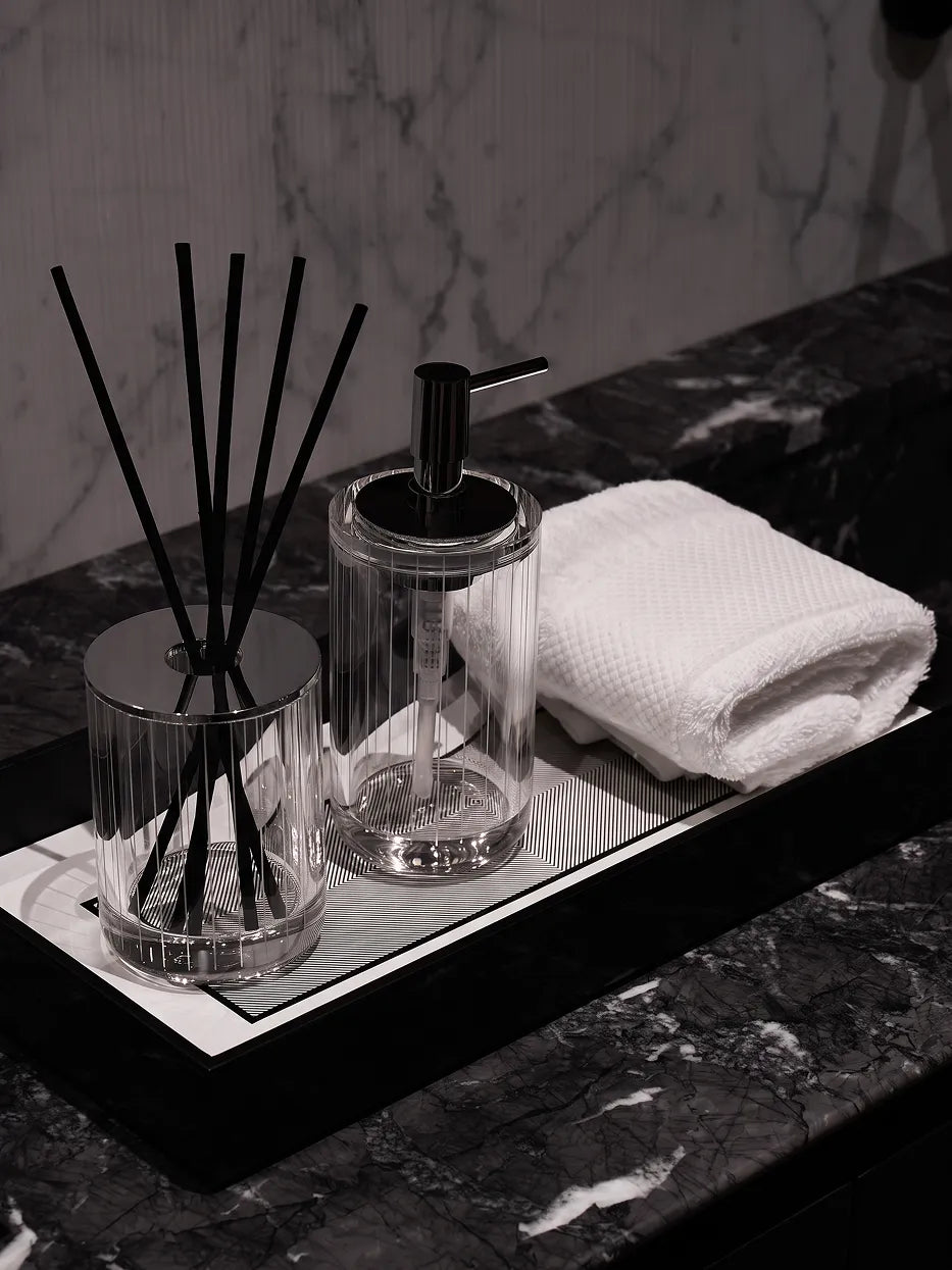 Monochrome minimalist bathroom furnishing shot of XUYU lotion bottle matched with striped reed diffuser & white towel on dark grey marble vanity tray