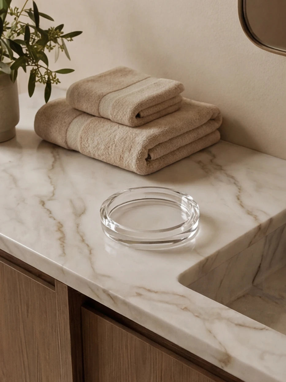 Soft home bathroom furnishing shot of single XUYU crystal soap dish on white-vein marble vanity counter with folded beige towel
