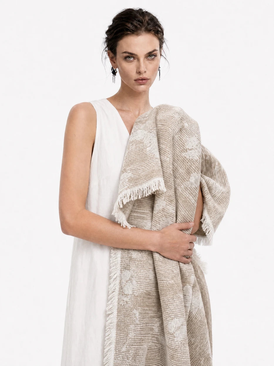 Minimalist full-body portrait shot of model holding YUNQI beige jacquard linen striped throw, fully displays overall blanket silhouette, complete vertical floral jacquard layout and bottom fringe design, dual function as decorative home couch cover and wearable shawl for indoor & outdoor use