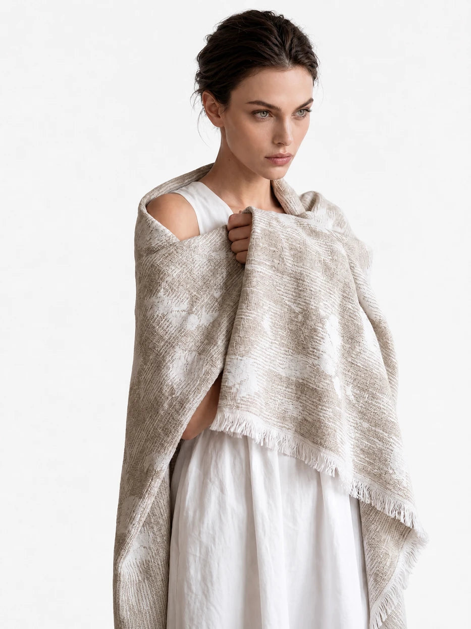 Pure white background half portrait shot of model wrapped with YUNQI beige jacquard linen blanket, demonstrates multi-scene usage as wearable shawl, office nap cover, outdoor beach wrap, lightweight breathable linen wool blend fabric suitable for all seasons, minimalist wearable home textile for daily rest and travel